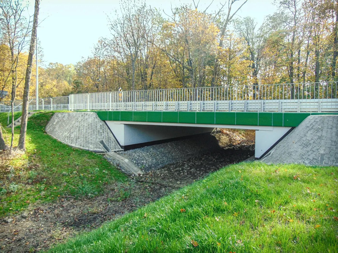 Most z zielonym pasem elewacyjnym, konstrukcja nad rowem w terenie leśnym